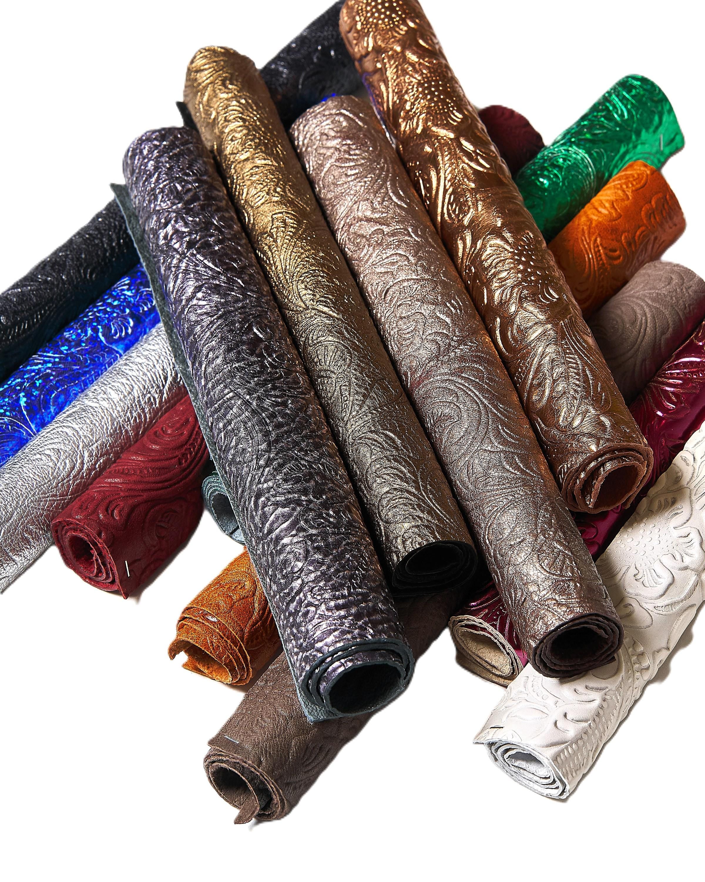 Può includere: Una collezione di fogli di pelle goffrata arrotolati in vari colori. L'assortimento comprende nero, argento, oro, marrone, rosso, verde e bianco. Ogni rotolo mostra un motivo floreale dettagliato, offrendo una superficie tattile e decorativa.
