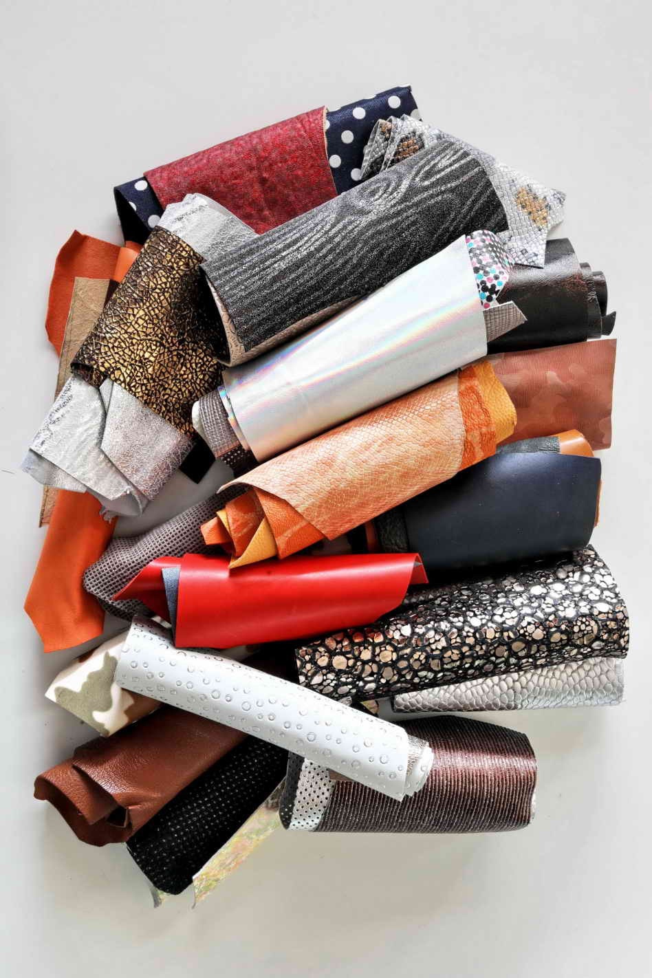 Può includere: Un mucchio di ritagli di tessuto di diversi colori e motivi, tra cui nero, bianco, marrone, rosso, arancione e oro. I ritagli sono arrotolati e disposti in modo casuale.
