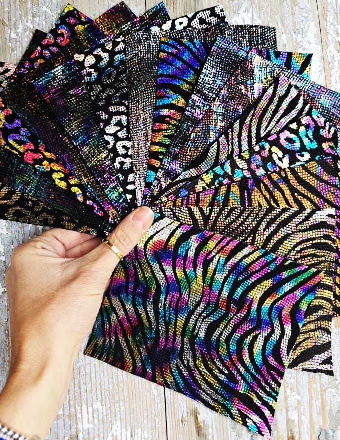 Può includere: Una collezione di campioni di tessuto iridescente con disegni di stampa animalier, tra cui motivi zebrati, leopardati e ghepardati. Il tessuto ha una finitura testurizzata e scintillante.