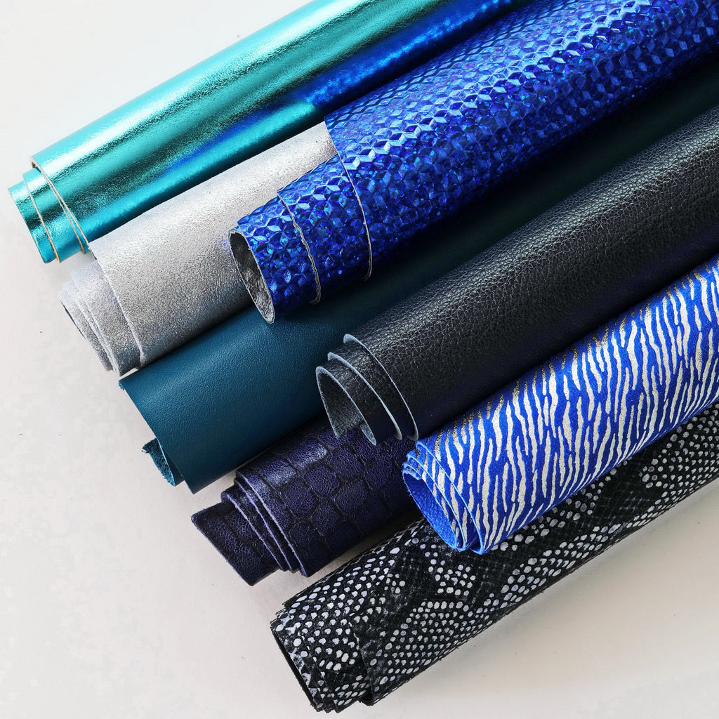 Può includere: Una collezione di diversi tessuti testurizzati in tonalità di blu, nero e argento. I tessuti sono disposti in una pila, con il tessuto superiore che è un materiale blu lucido.