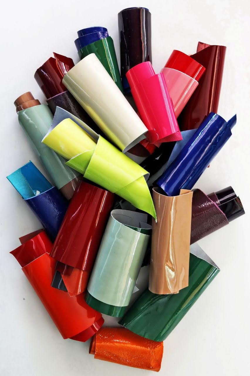 Può includere: Una collezione di rotoli di vinile colorati in varie tonalità di rosso, verde, blu, giallo, marrone e bianco. I rotoli sono disposti in una pila, con alcuni di essi sovrapposti.