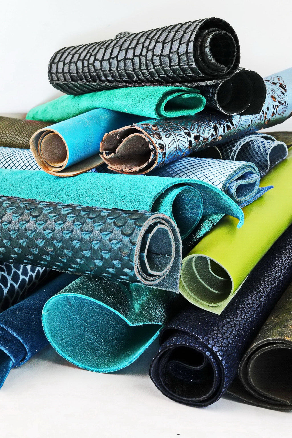 Può includere: Una collezione di pezzi di pelle arrotolati in vari colori e trame, tra cui blu, verde, nero e marrone. La pelle è disposta in una pila, con alcuni pezzi sovrapposti.