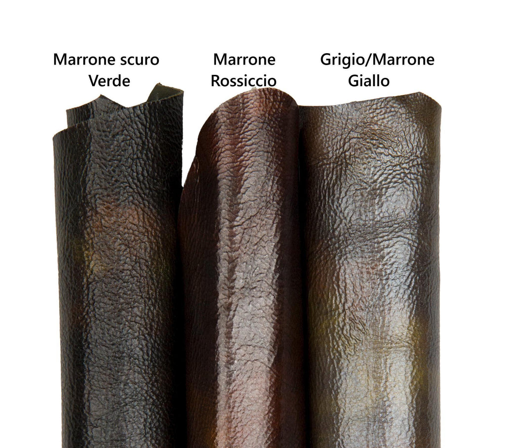 Può includere: Primo piano di tre campioni di pelle arrotolati in tonalità marroni e verdi. I campioni sono etichettati con testo italiano: "Marron scuro Verde", "Marron Rossiccio" e "Grigio/Marron Giallo". La pelle ha una superficie strutturata.