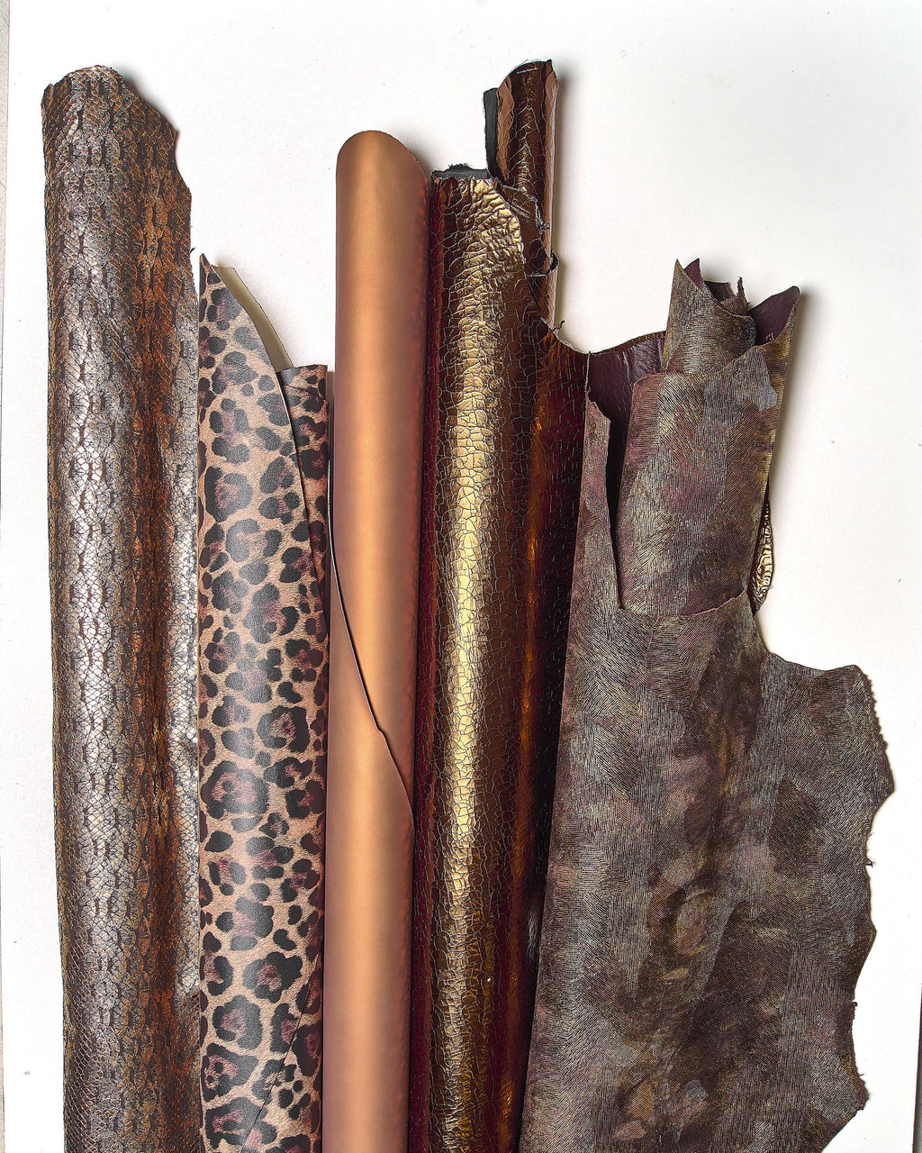 Può includere: Una collezione di pelli di cuoio arrotolate e piatte in vari modelli e colori. Le pelli includono texture a pelle di serpente, stampa leopardata e tonalità bronzo e marrone tinta unita. Le trame variano da lisce a goffrate, mostrando la diversità dei materiali in pelle.