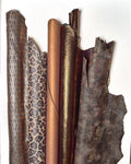 Può includere: Una collezione di pelli di cuoio arrotolate e piatte in vari modelli e colori. Le pelli includono texture a pelle di serpente, stampa leopardata e tonalità bronzo e marrone tinta unita. Le trame variano da lisce a goffrate, mostrando la diversità dei materiali in pelle.
