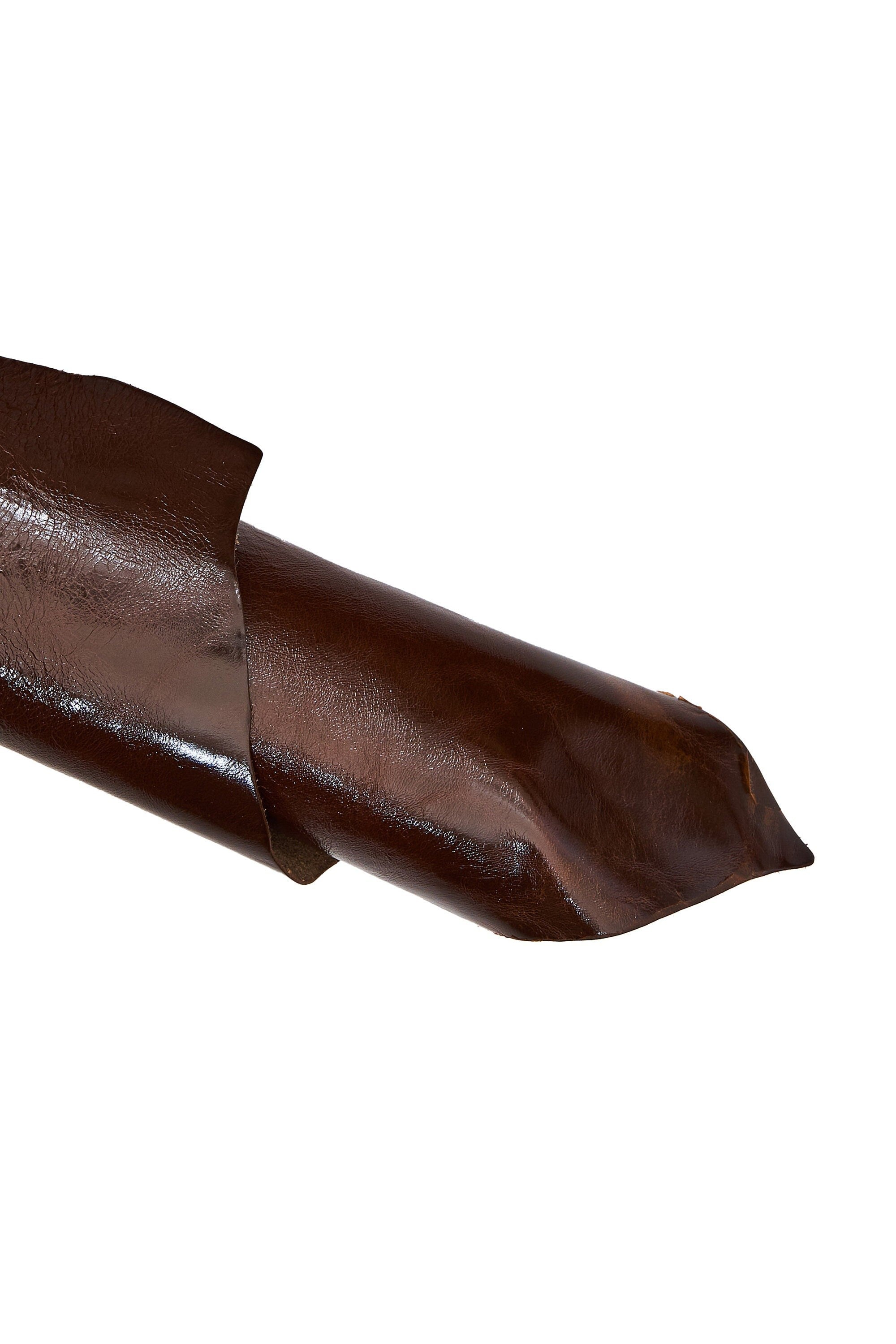 Può includere: Primo piano di un pezzo di pelle marrone scuro, piegato e curvo. La pelle ha una finitura lucida e una consistenza liscia con sottili variazioni. I bordi sono visibili, mostrando lo spessore e la forma del materiale.