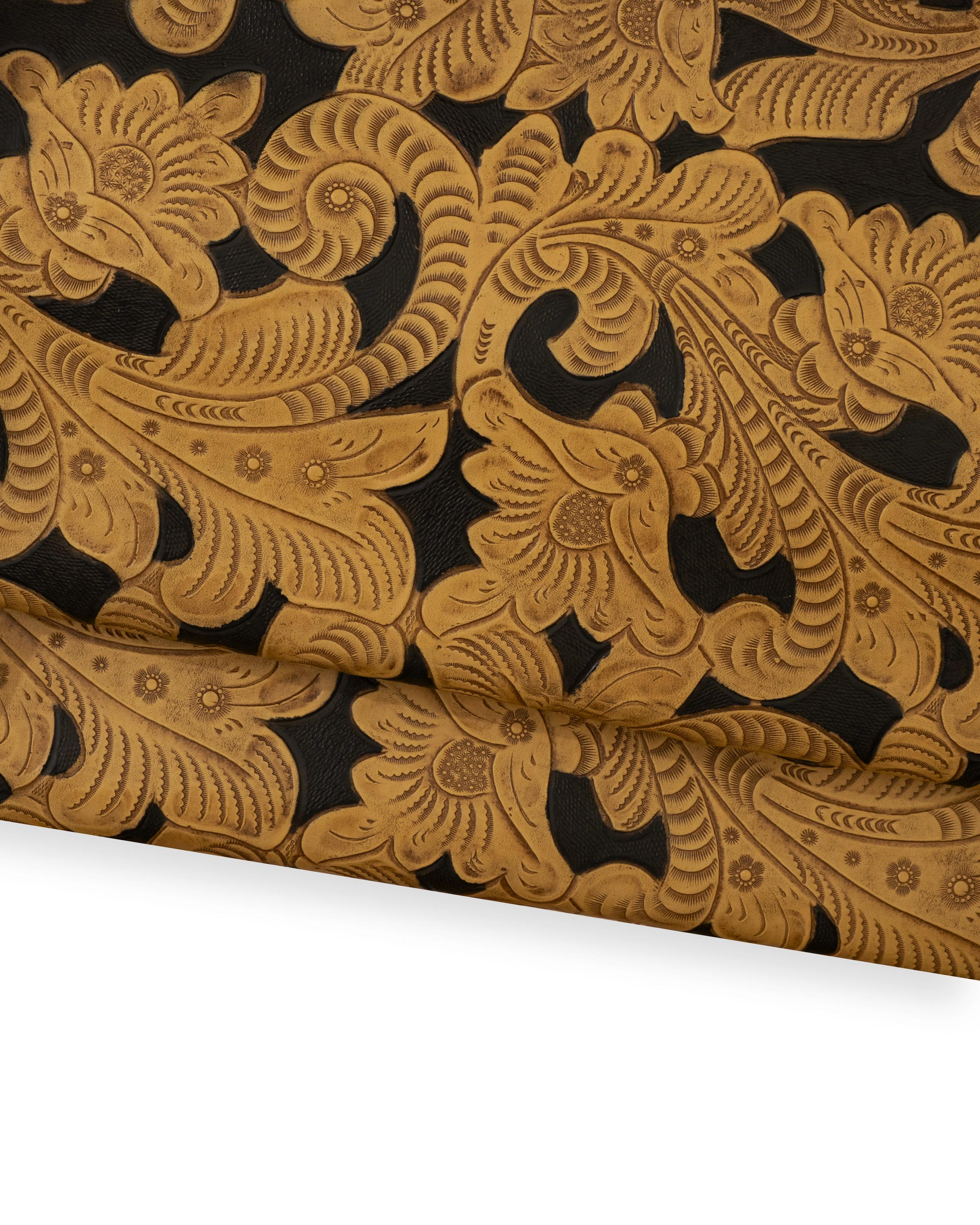 Può includere: Primo piano di un materiale in pelle con un motivo floreale dettagliato. Il design presenta fiori in rilievo e foglie vorticose in tonalità beige e marrone su uno sfondo nero. La trama della pelle è visibile, evidenziando l'artigianalità.