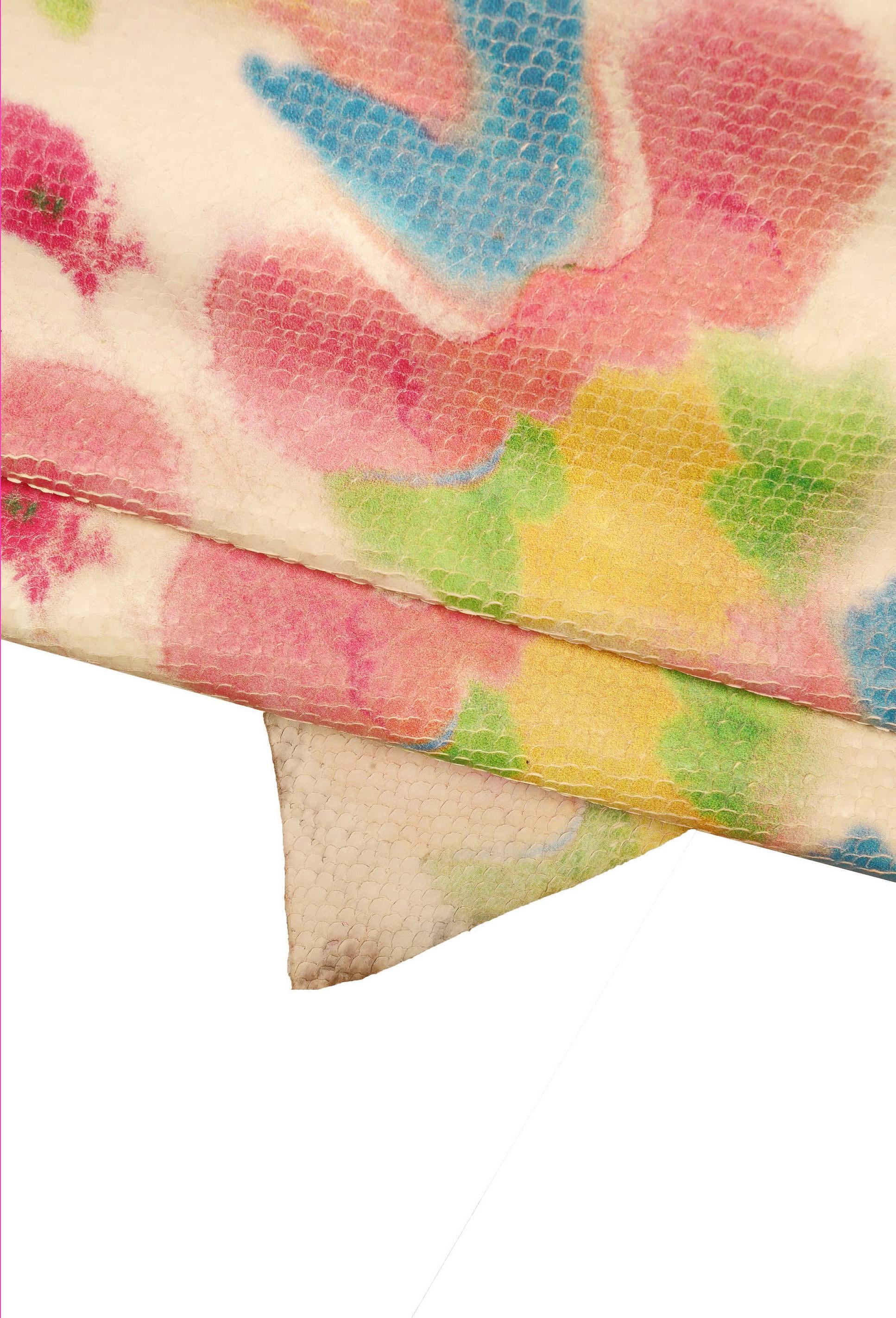 Può includere: Primo piano di un tessuto con una superficie testurizzata e un motivo floreale colorato. Il tessuto è piegato a metà, rivelando il motivo su entrambi i lati. I colori del motivo includono rosa, blu, giallo e verde.