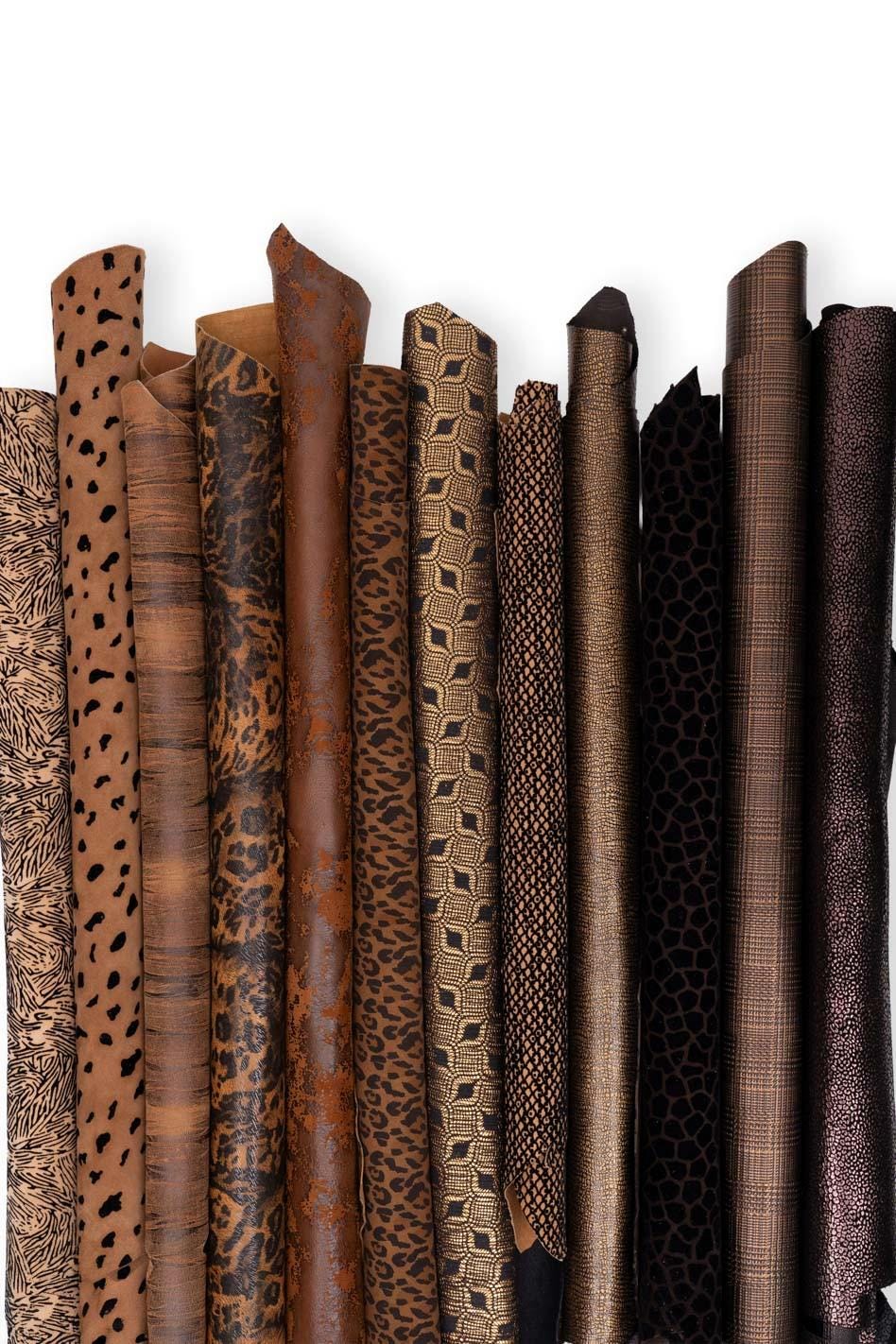 Può includere: Una collezione di undici fogli di pelle arrotolati con vari motivi e texture nelle tonalità del marrone, beige, nero e bronzo. L'assortimento comprende stampe animalier, disegni geometrici, motivi scozzesi e finiture metalliche.