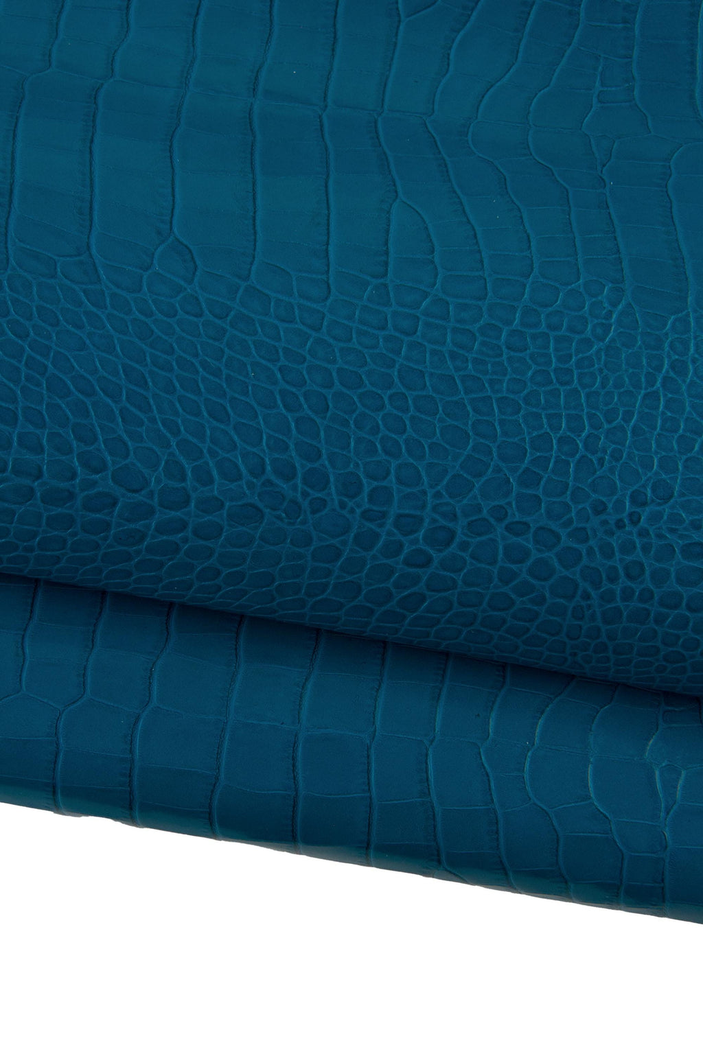 May include: Close-up of teal-colored leather with a crocodile skin texture. The leather is folded, revealing the detailed pattern of scales and ridges. The color is a deep, saturated teal, with subtle variations in tone.