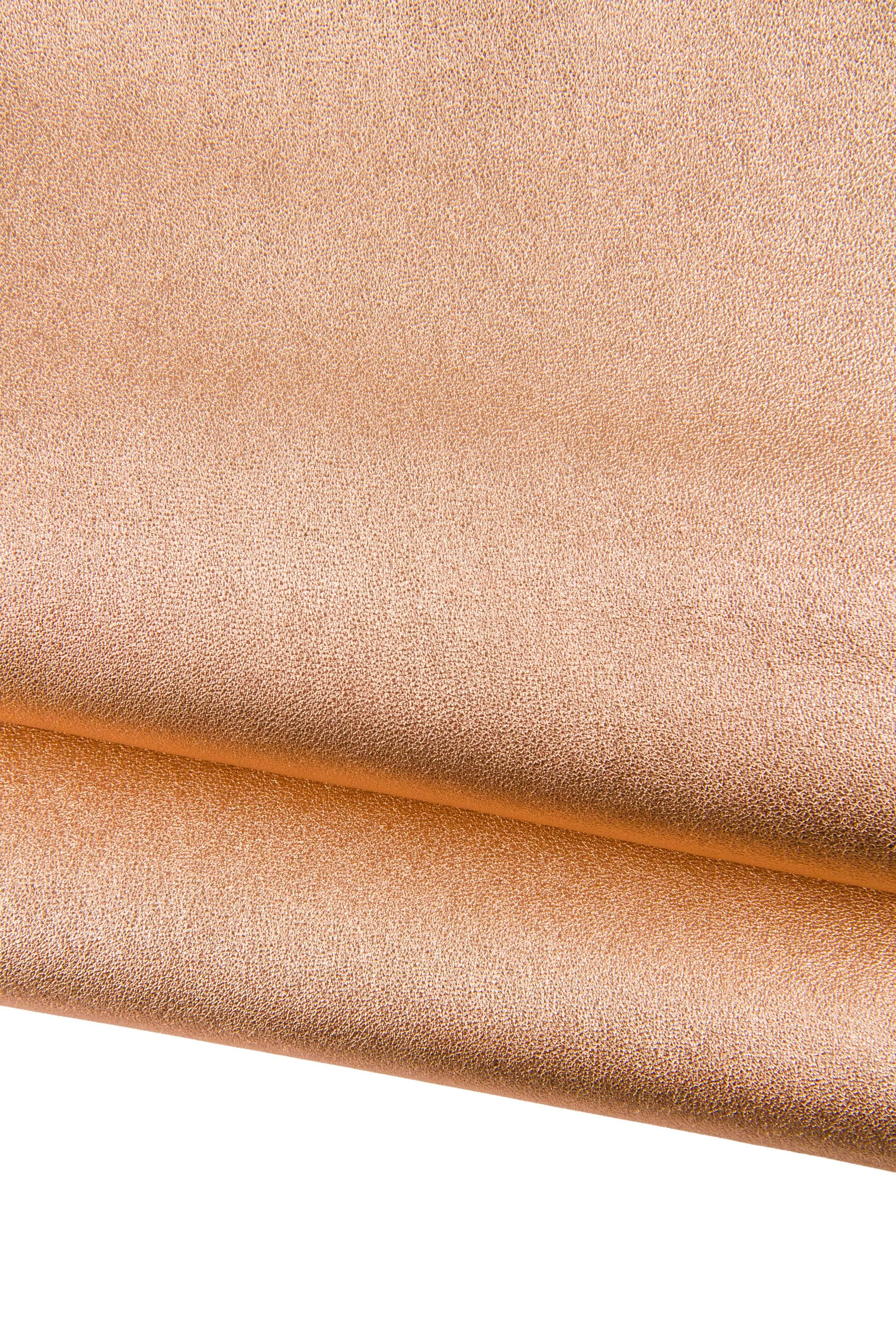 Può includere: Primo piano di un tessuto strutturato con un aspetto metallico in un caldo color rame. Il materiale è piegato, rivelando uno scorcio del lato inferiore. La superficie presenta un motivo sottile e maculato, che suggerisce pelle o similpelle. Ideale per progetti di artigianato o moda.