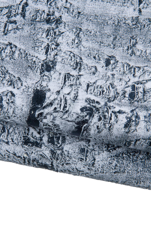 Può includere: Primo piano di materiale strutturato con un aspetto invecchiato e screziato. La superficie è prevalentemente bianca con accenti grigio scuro e neri, creando una texture ruvida, quasi simile alla pietra. Il materiale sembra essere piegato o stratificato.