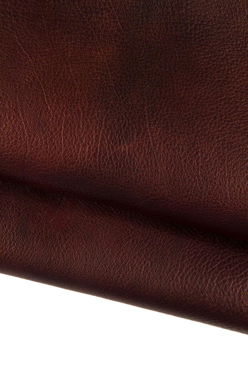Può includere: Primo piano di una texture in pelle marrone scuro con un sottile motivo granulare. La pelle è piegata, mostrando la sua flessibilità e la profondità del colore.