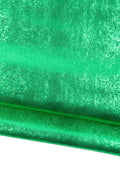May include: Close-up of a vibrant green fabric with a textured, reptile-like pattern. The material has a metallic sheen, reflecting light and creating a shimmering effect. The fabric is folded, revealing its layered structure.