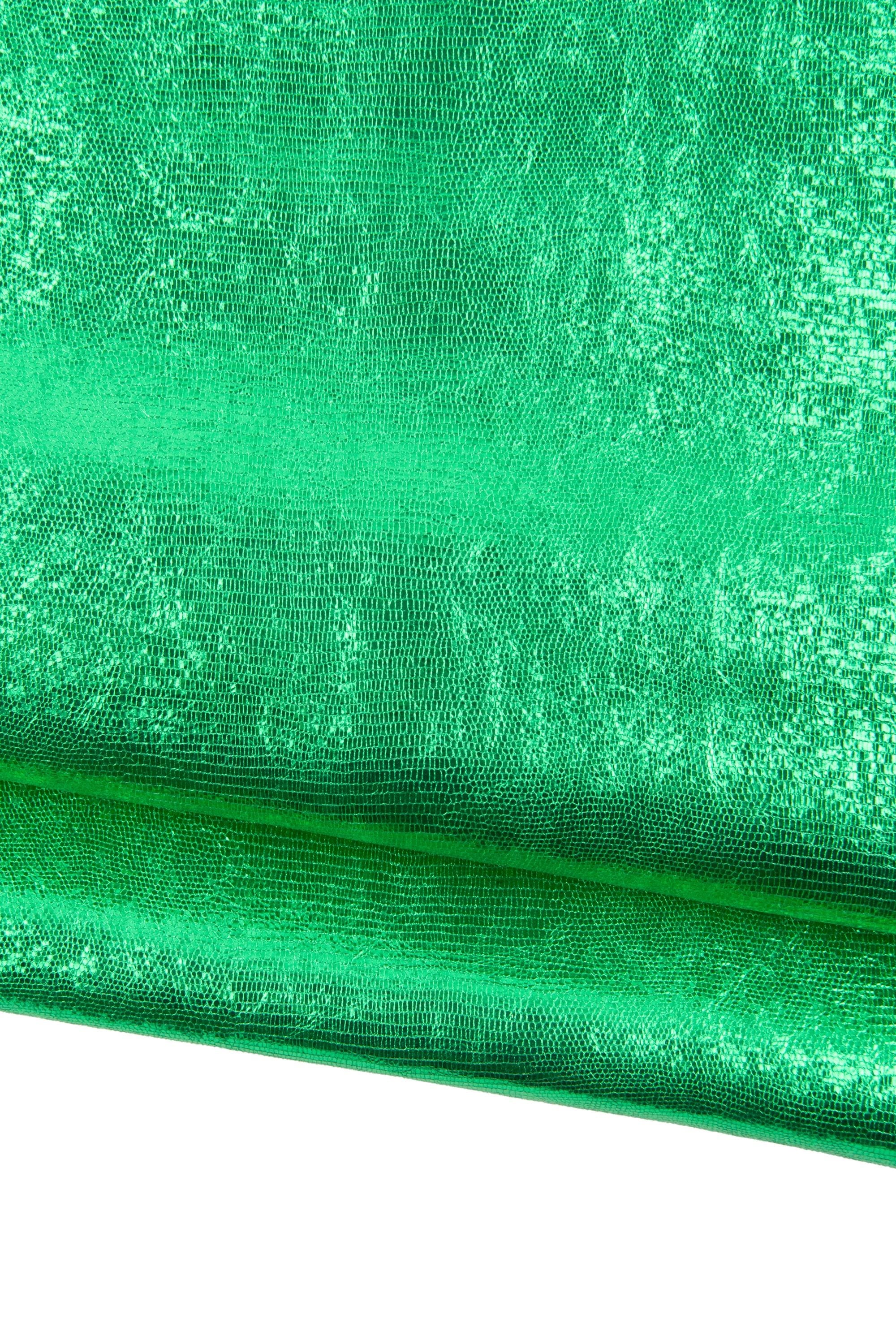 May include: Close-up of a vibrant green fabric with a textured, reptile-like pattern. The material has a metallic sheen, reflecting light and creating a shimmering effect. The fabric is folded, revealing its layered structure.
