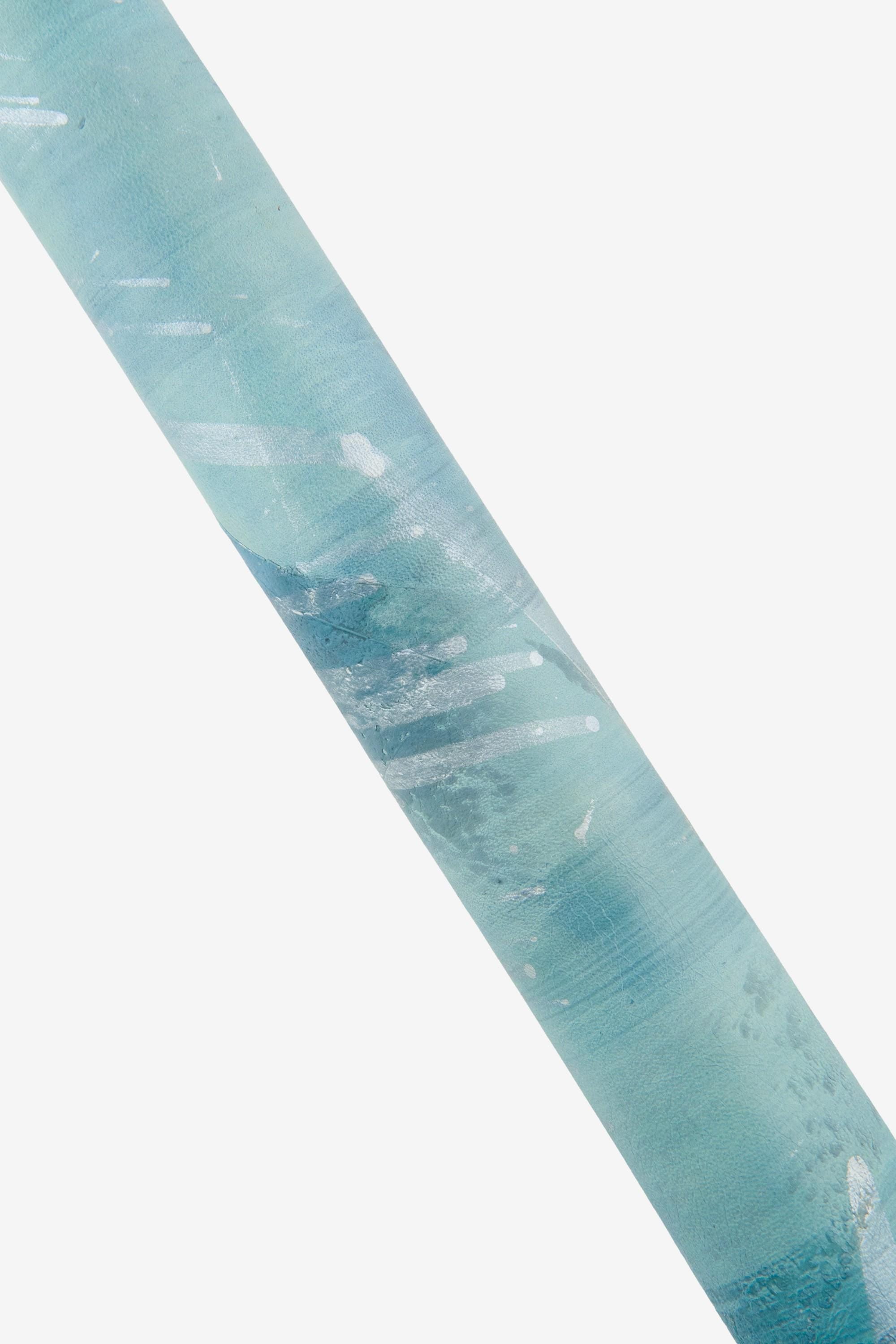 Può includere: Vista angolata di un rotolo di carta per acquerello blu e verde acqua. La carta ha una superficie strutturata con schizzi e striature di vernice bianca. La carta è posizionata diagonalmente su uno sfondo bianco.