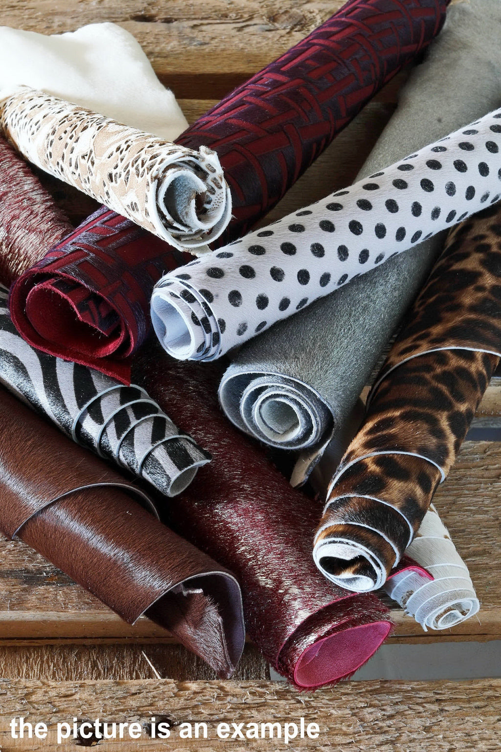 Può includere: Un assortimento di campioni di tessuto arrotolati in diversi colori e motivi, tra cui stampa leopardata, stampa zebra, pois e colori solidi. I campioni sono disposti su una superficie di legno.
