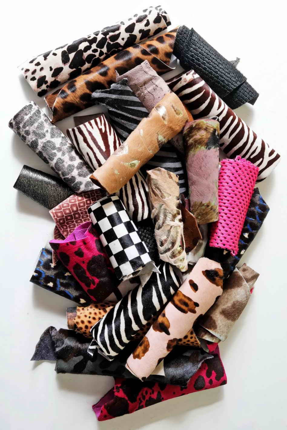 Può includere: Una collezione di ritagli di pelle colorati e con motivi, tra cui stampe zebrate, leopardo e ghepardo, oltre a quadri e colori solidi. I ritagli sono arrotolati e disposti in una pila.
