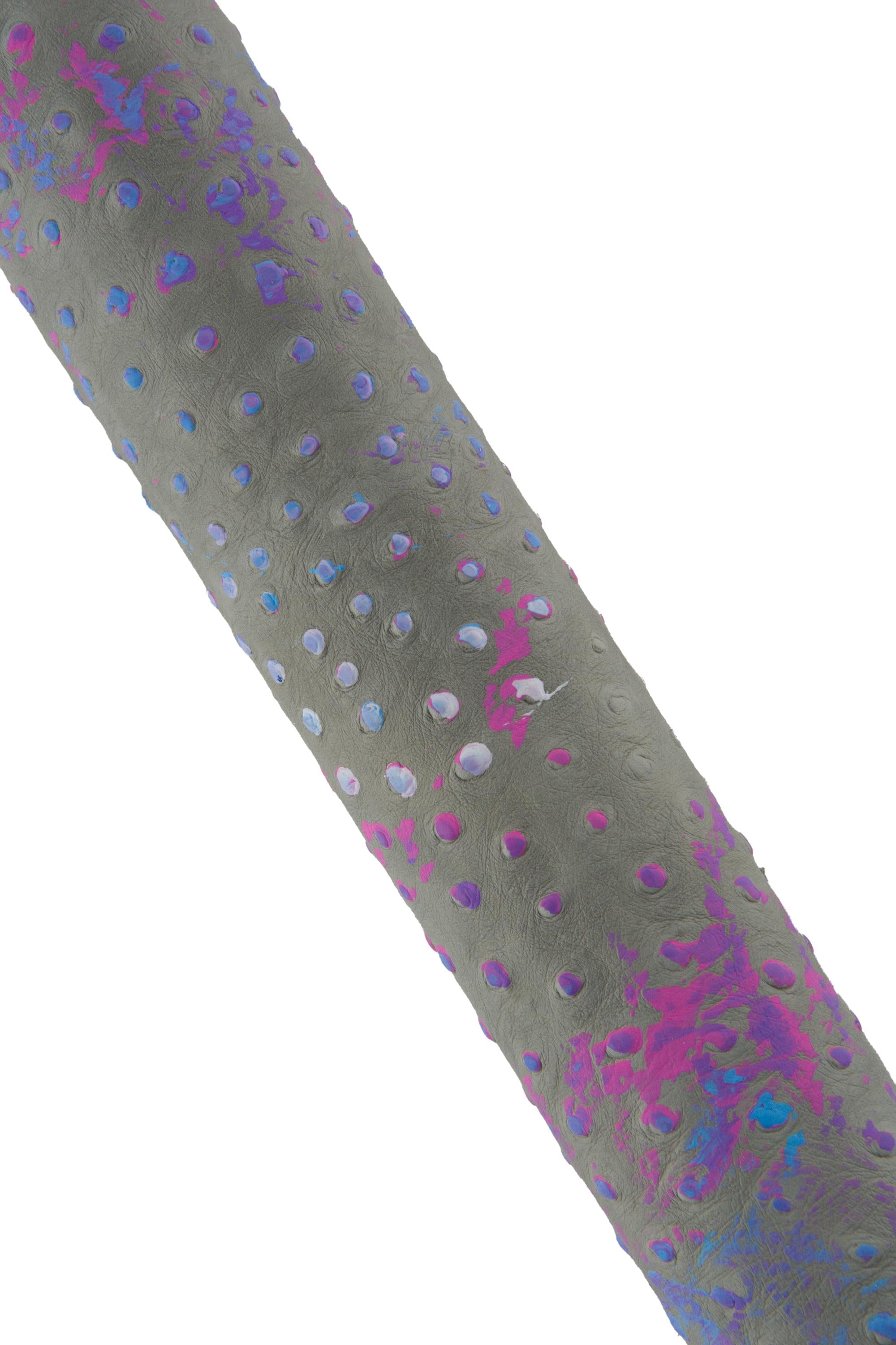 Può includere: Primo piano di un oggetto cilindrico strutturato con un colore di base grigio. La superficie è punteggiata da piccoli fori distanziati uniformemente. Macchie di tonalità rosa, viola e blu sono sparse sulla superficie, aggiungendo un tocco di colore.