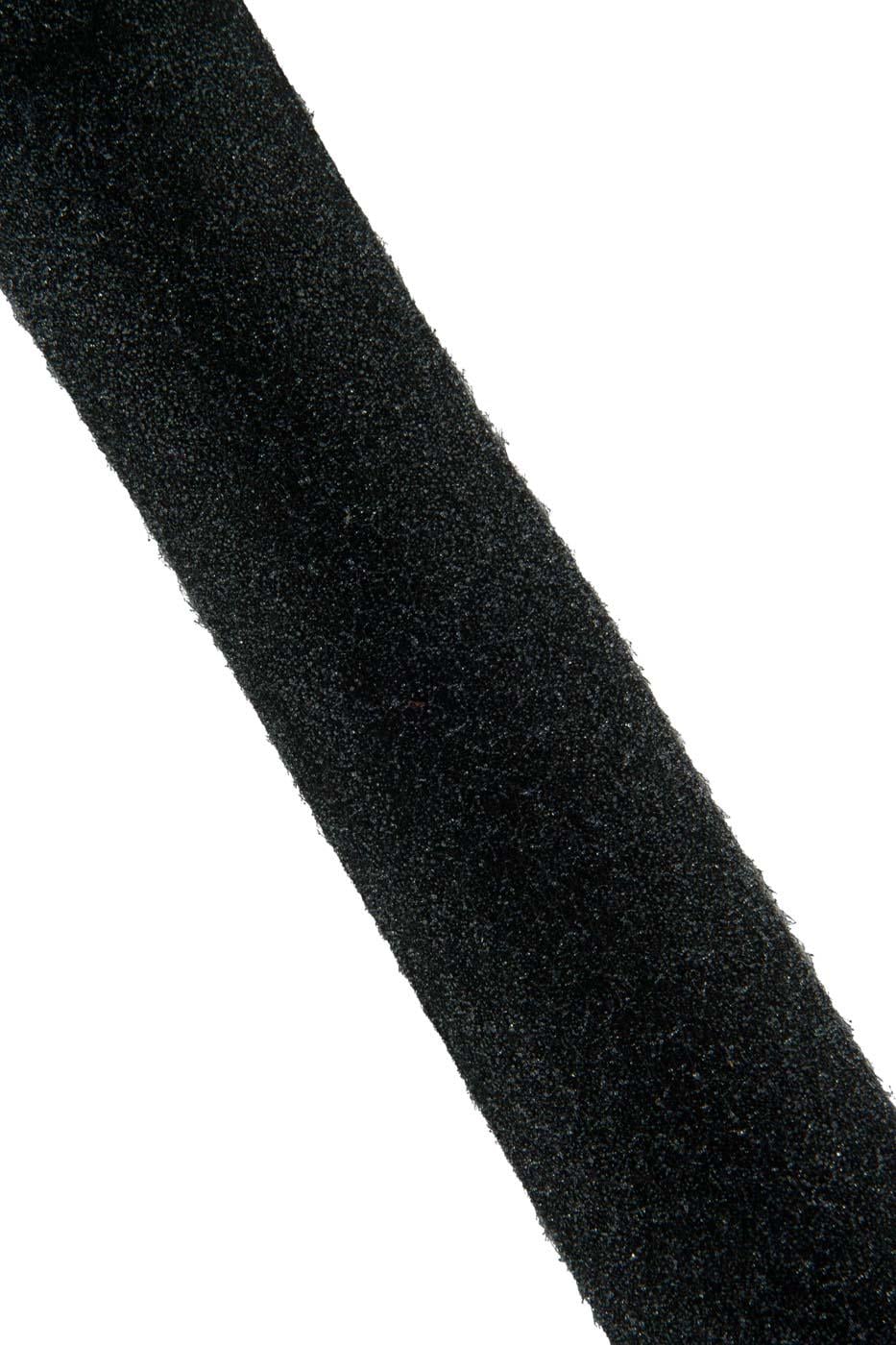 Può includere: Una lunga e stretta striscia di materiale nero con una superficie ruvida e opaca. La striscia è posizionata diagonalmente nell'inquadratura, mostrando una larghezza costante e un bordo leggermente sfilacciato e fibroso su entrambi i lati.