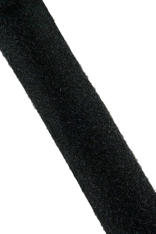 Può includere: Una lunga e stretta striscia di materiale nero con una superficie ruvida e opaca. La striscia è posizionata diagonalmente nell'inquadratura, mostrando una larghezza costante e un bordo leggermente sfilacciato e fibroso su entrambi i lati.