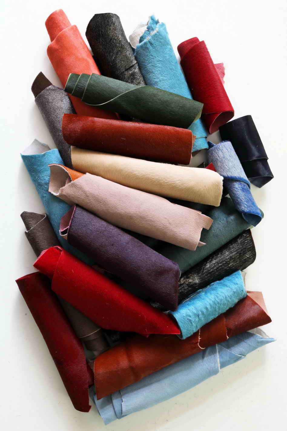 Può includere: Una collezione di ritagli di pelle di vari colori, tra cui rosso, blu, marrone e nero. La pelle è arrotolata e disposta in un mucchio.
